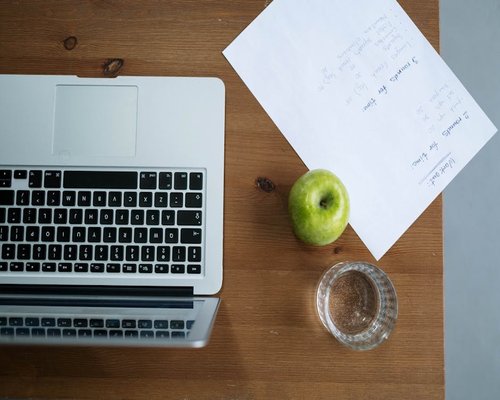 Person working on a laptop with a glass of water and a healthy snack nearby